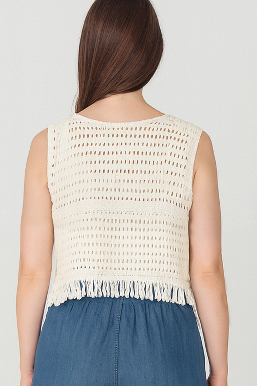 Woman wearing a beige crochet top with fringe details on a plain background
