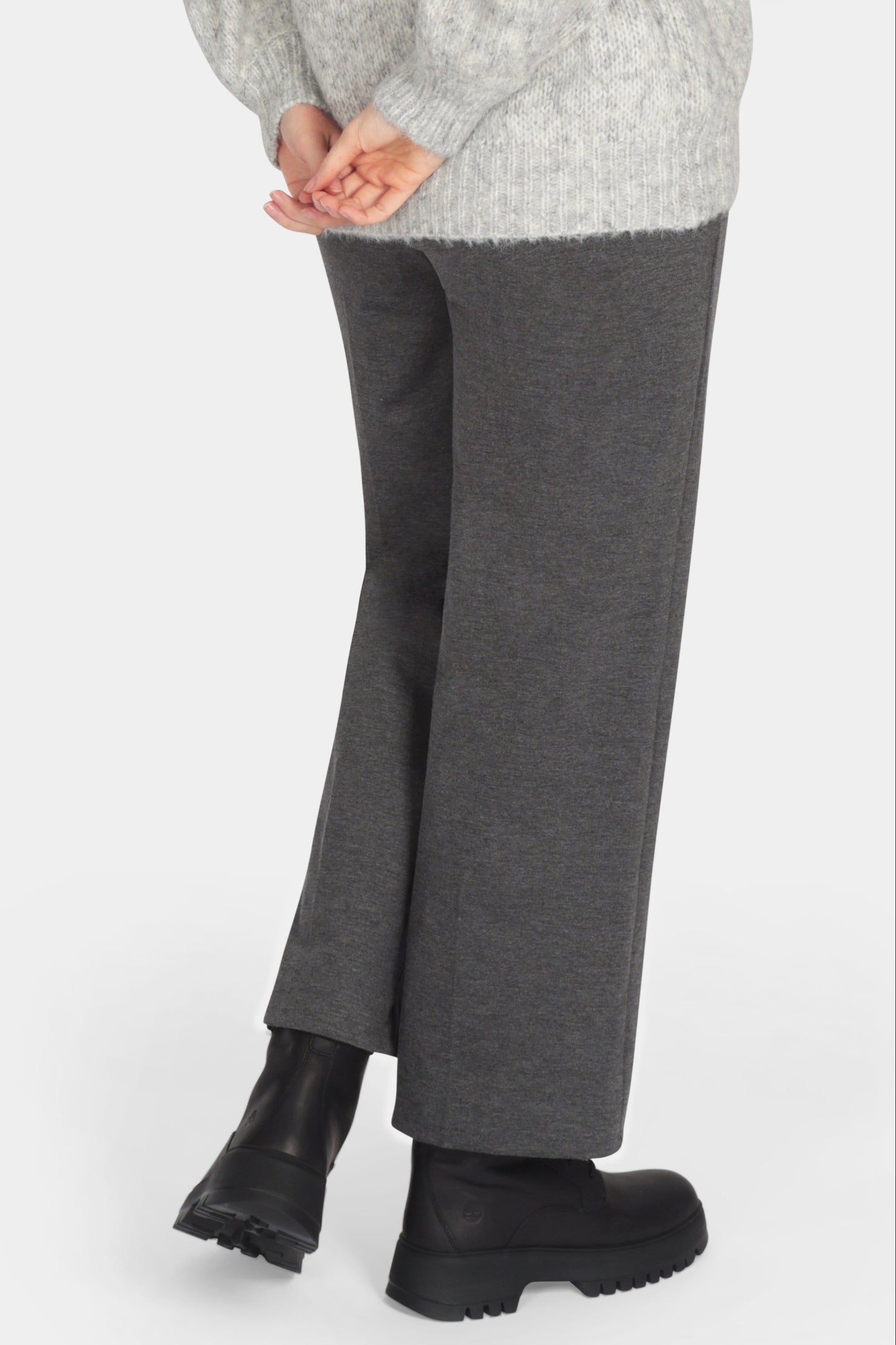 Woman wearing a gray sweater and dark gray pants on a white background