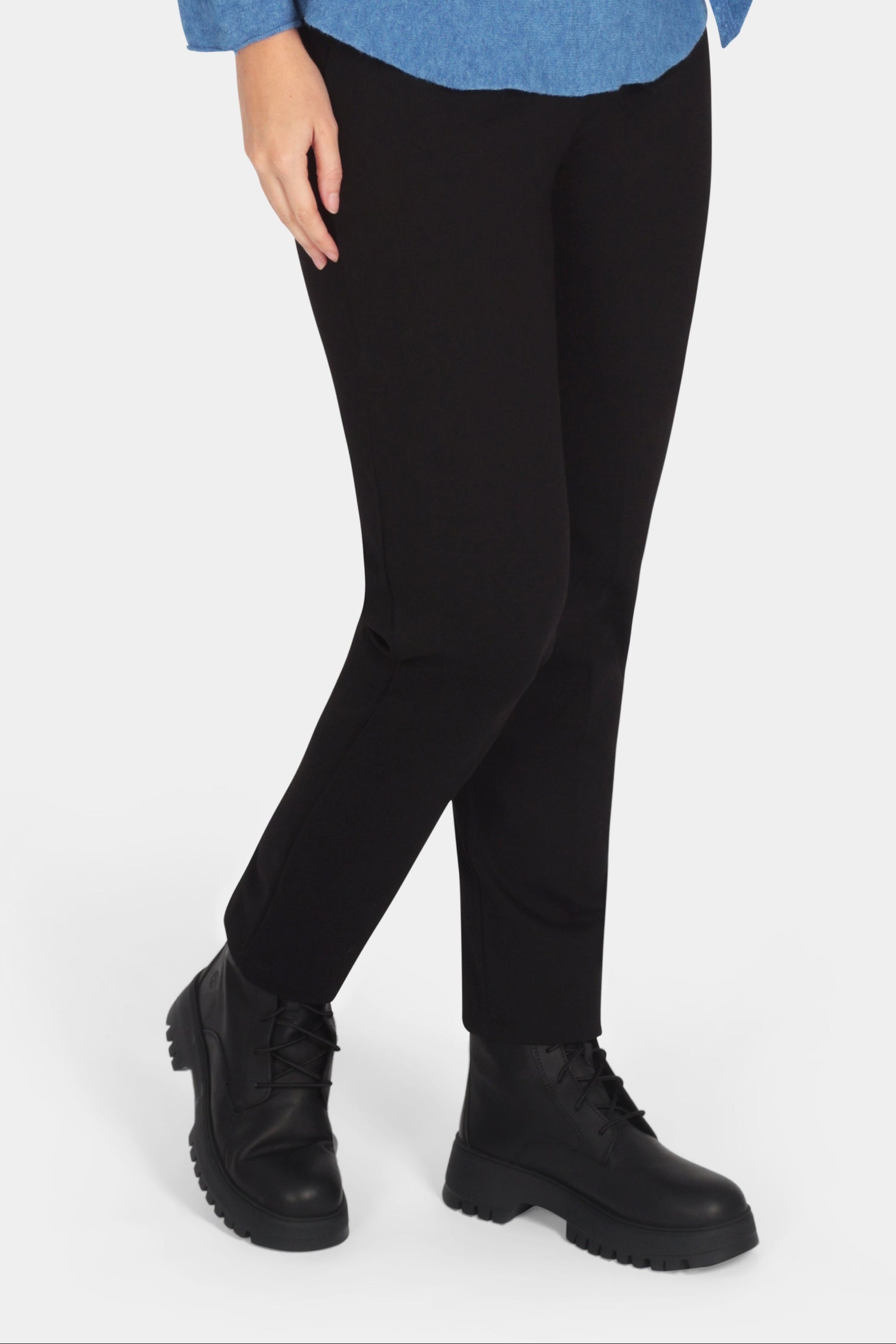 Woman wearing a blue sweater with a bow, black pants, and black boots on a white background