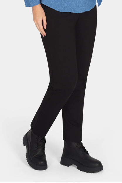 Woman wearing a blue sweater with a bow, black pants, and black boots on a white background