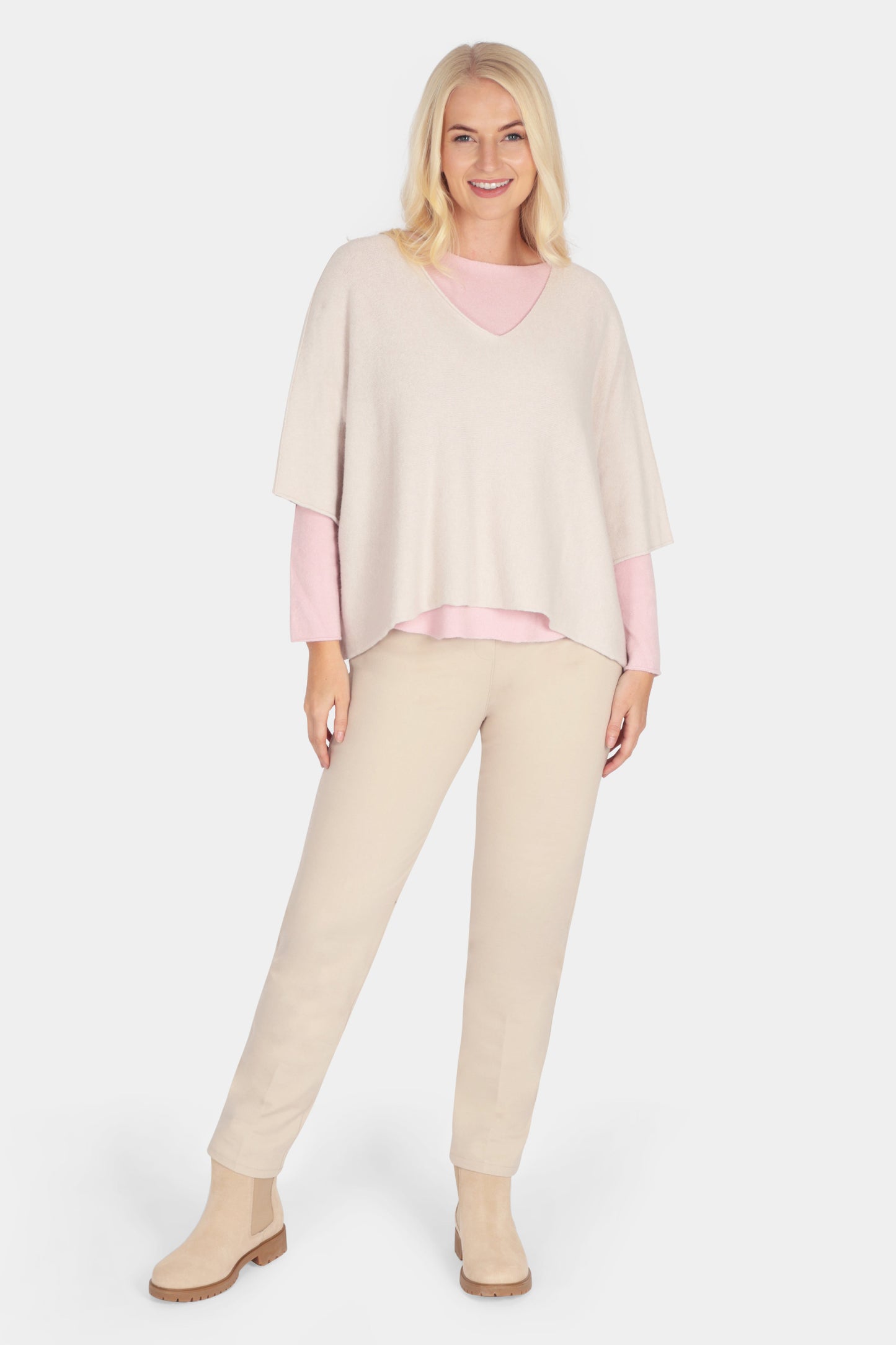 Woman wearing a light pink sweater and beige pants on a white background