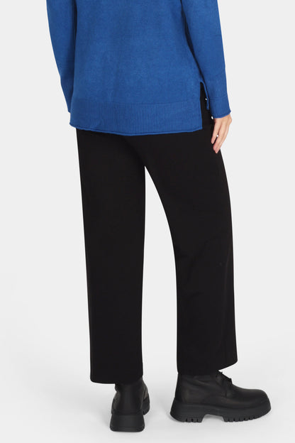 Person wearing a blue sweater and black pants on a white background