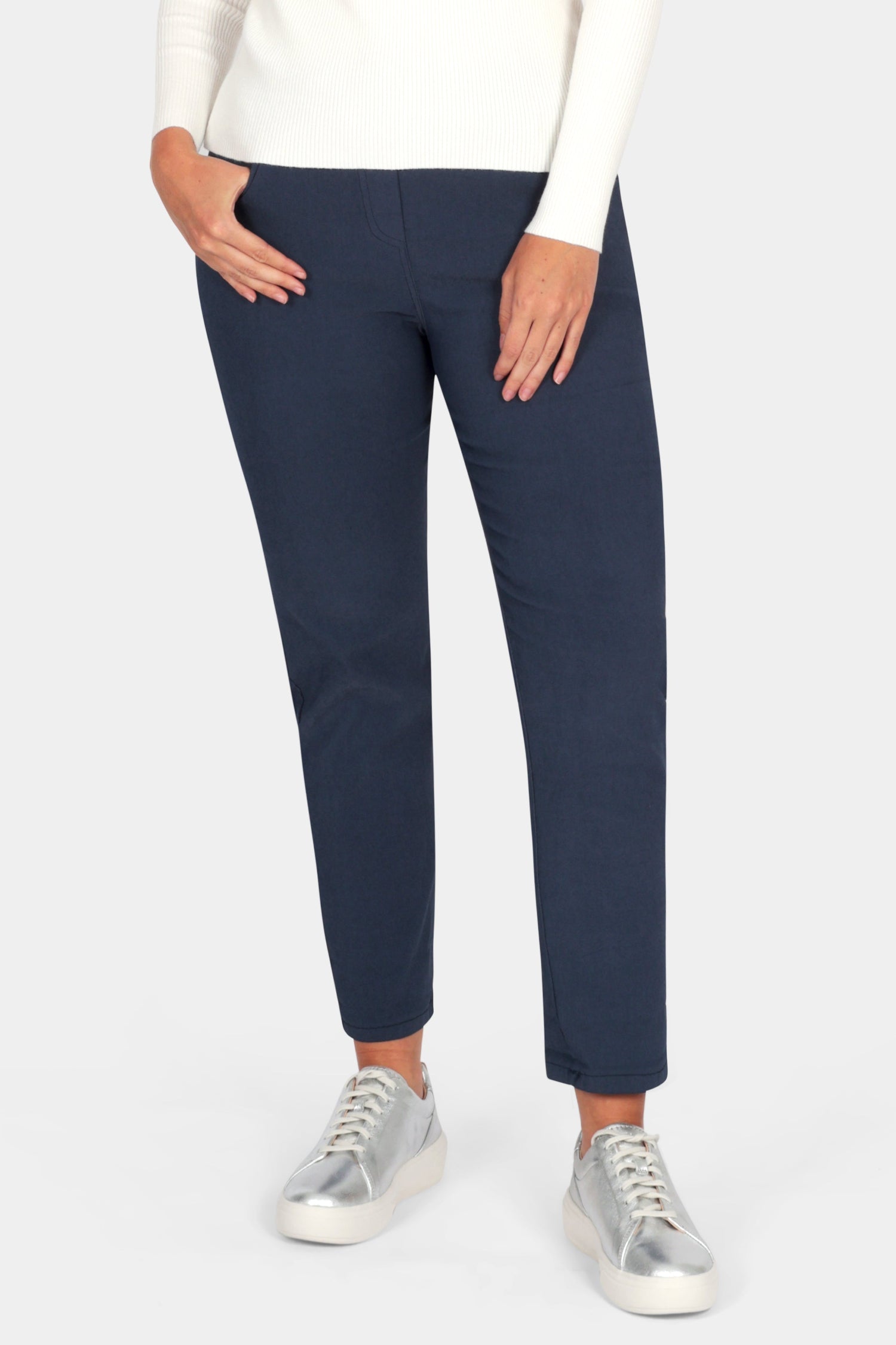 Woman wearing a white sweater and navy pants on a white background