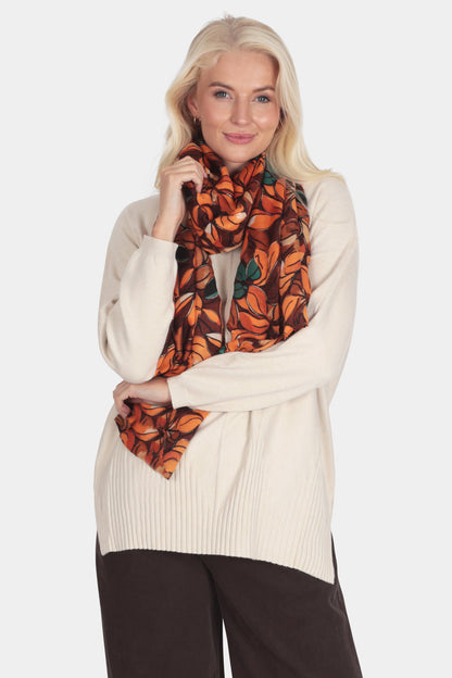 Woman wearing a cream sweater, brown pants, and a patterned scarf on a white background