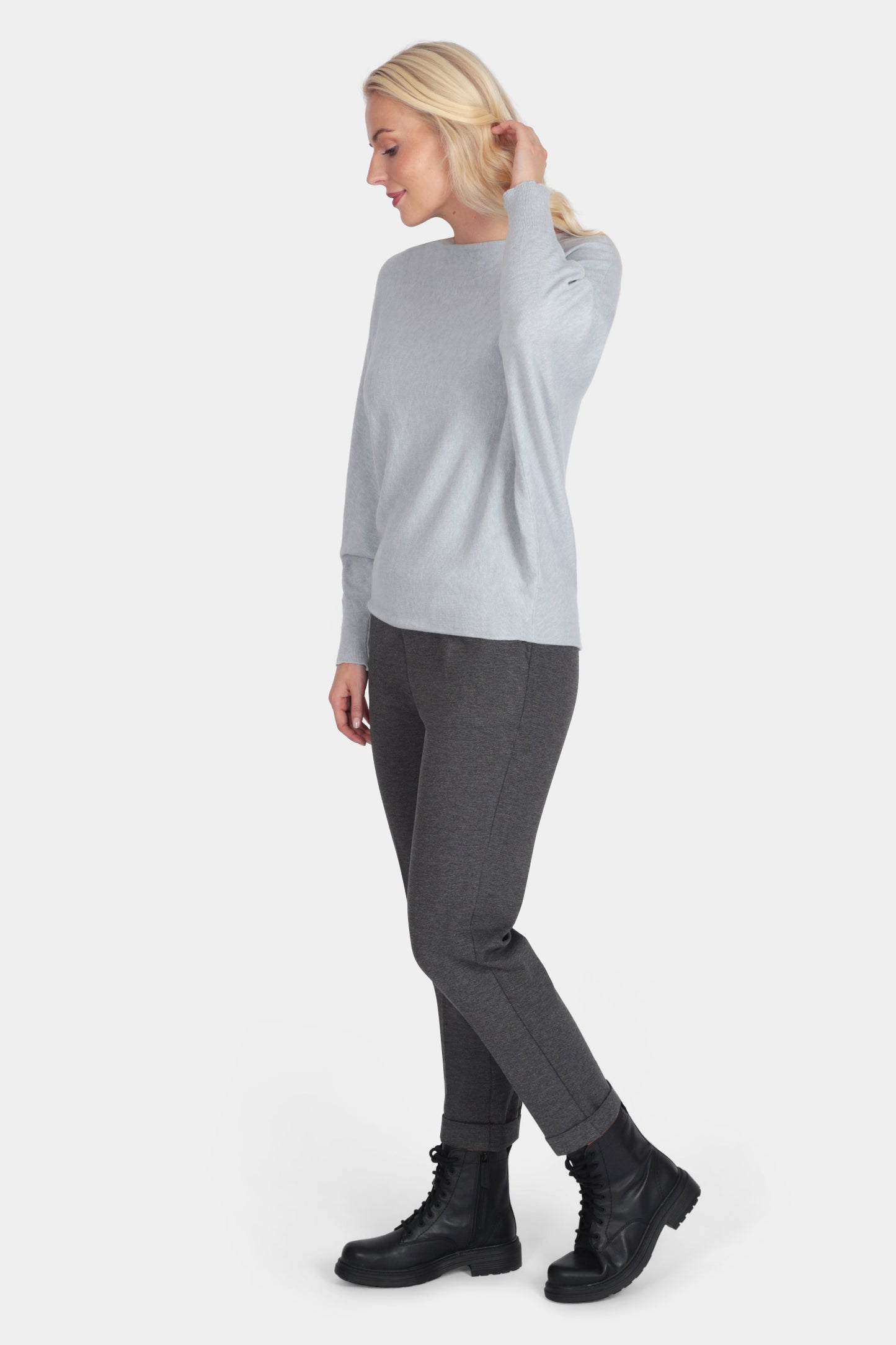 Woman wearing a light gray sweater and dark gray pants on a white background