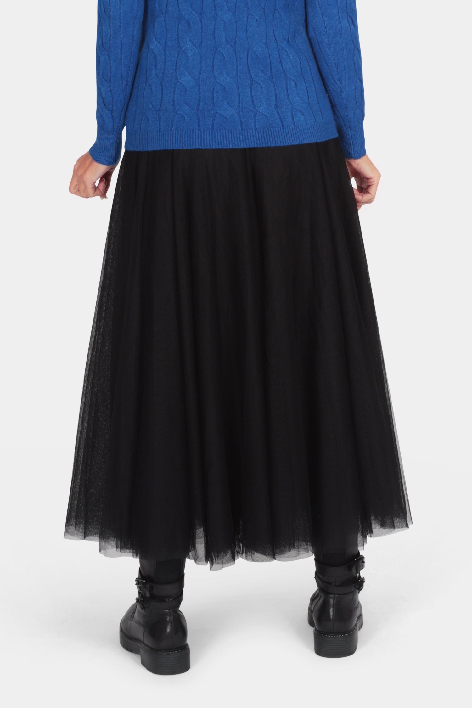 Person wearing a blue sweater and black skirt on a white background