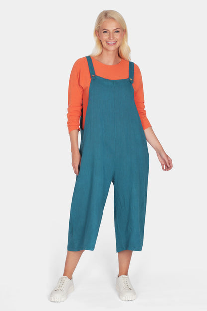 Woman wearing blue Artisan Linen Dungarees over an orange long sleeve top with white sneakers