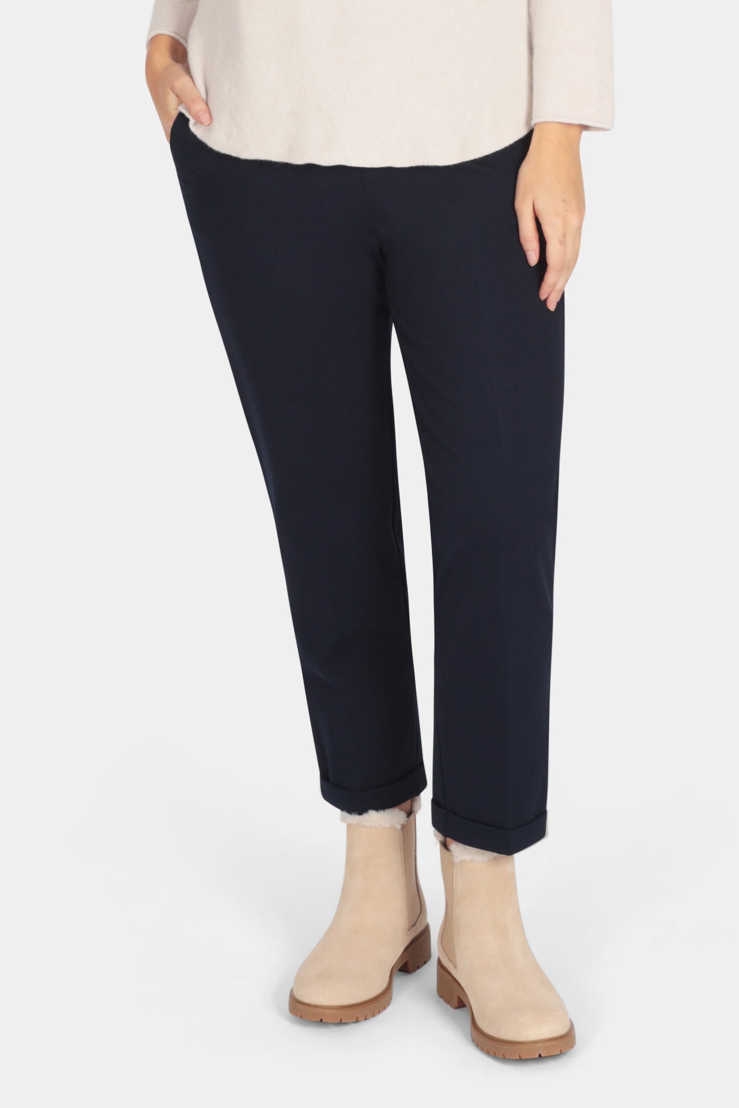 Woman wearing a beige sweater and navy pants on a white background