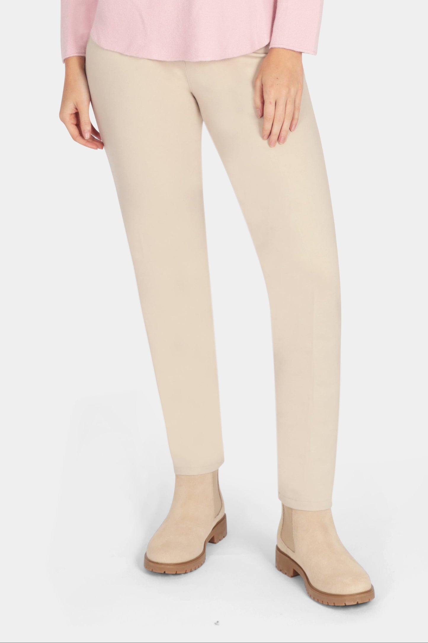 Woman wearing a pink sweater and beige pants on a white background