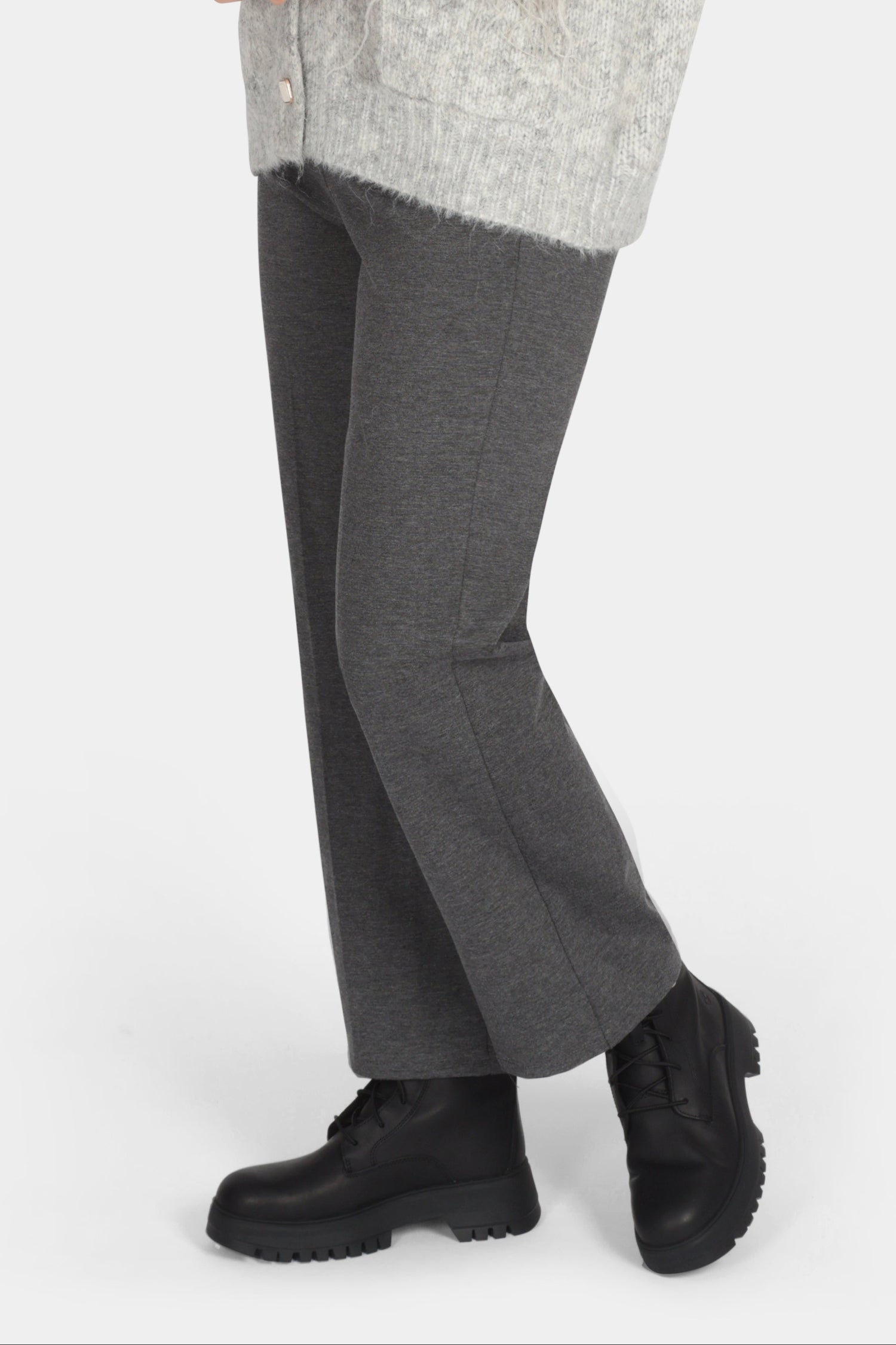 Woman wearing a gray cardigan, gray pants, and black shoes on a white background