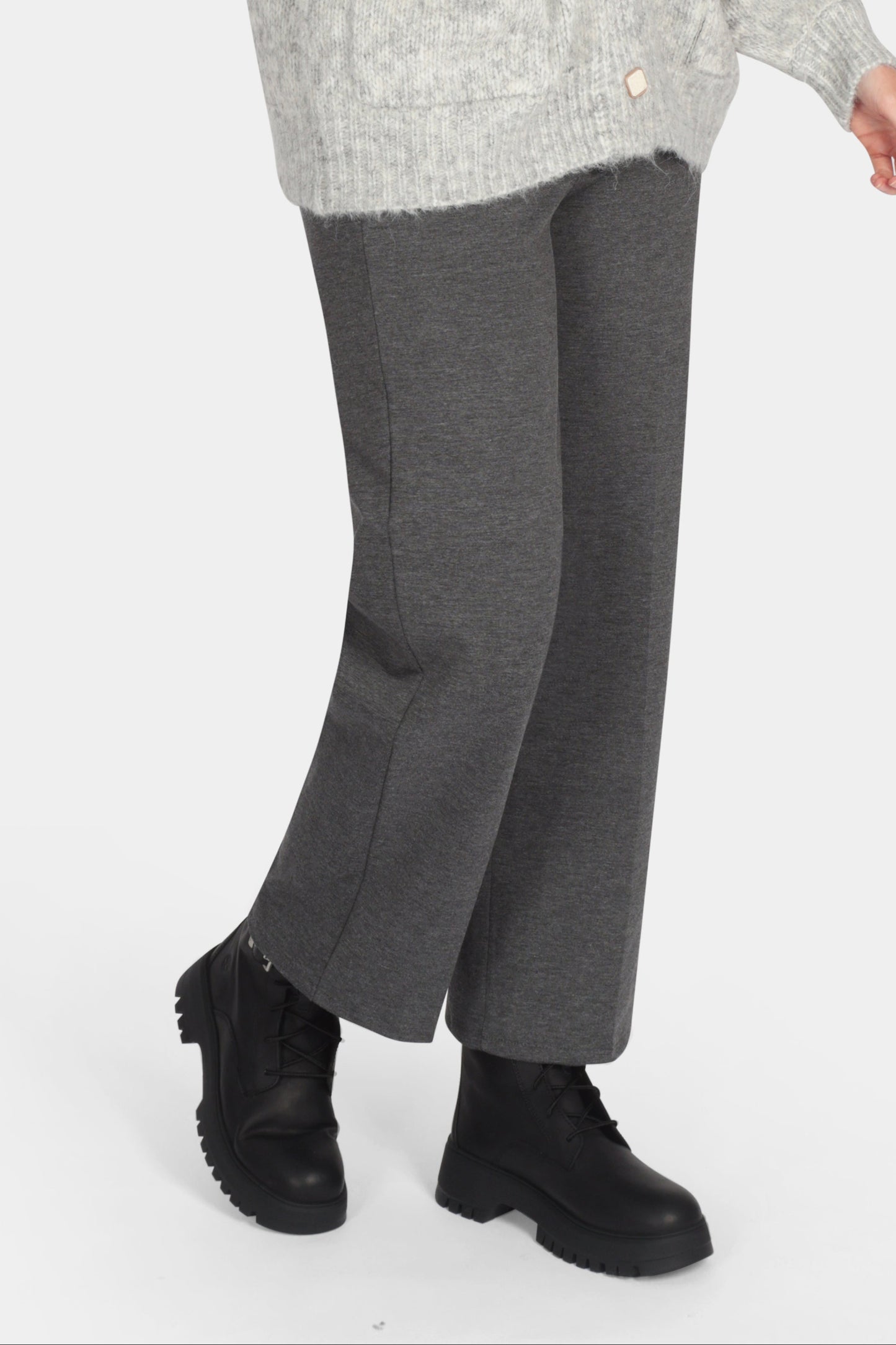 Woman wearing a gray cardigan, white shirt, gray pants, and black shoes on a white background