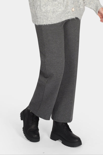 Woman wearing a gray cardigan, white shirt, gray pants, and black shoes on a white background