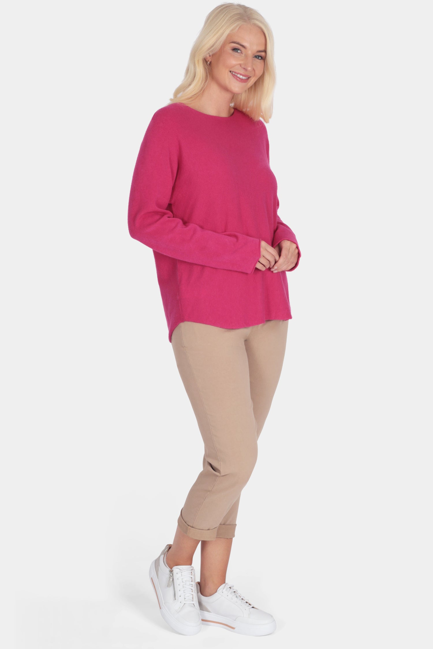 Woman wearing a bright pink sweater and beige pants on a white background