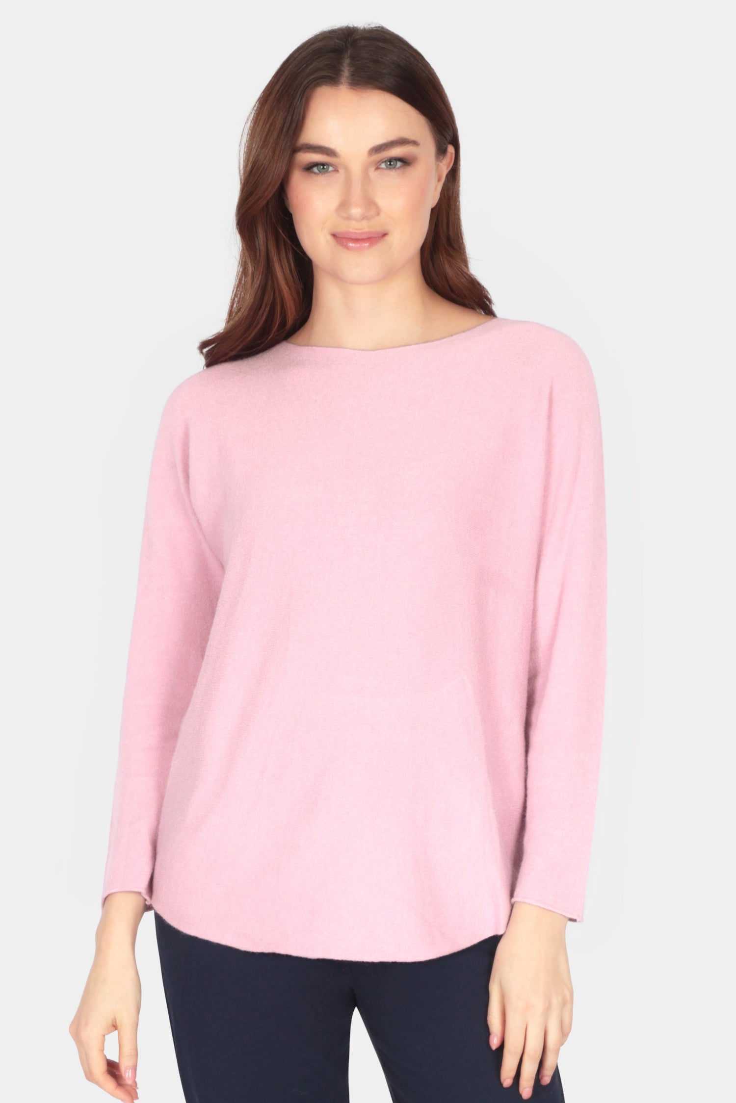Woman wearing a pink sweater and navy pants on a white background