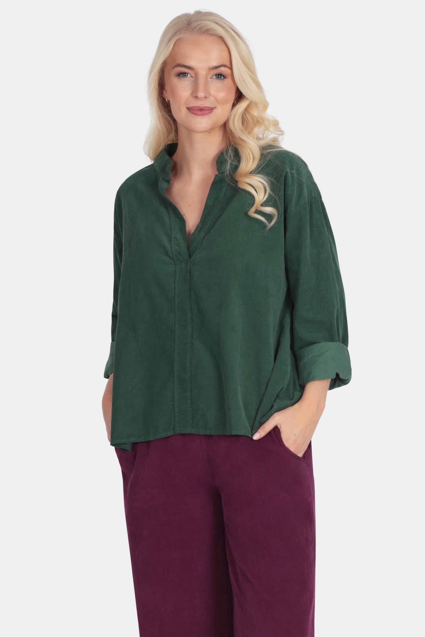 Woman wearing a green top and burgundy pants on a white background