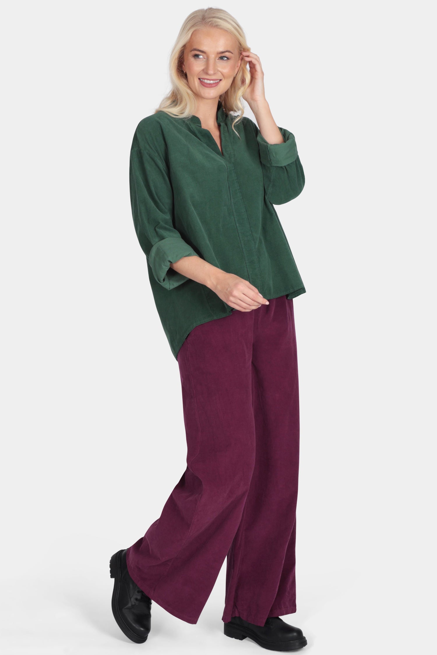 Woman wearing a green top and burgundy pants on a white background