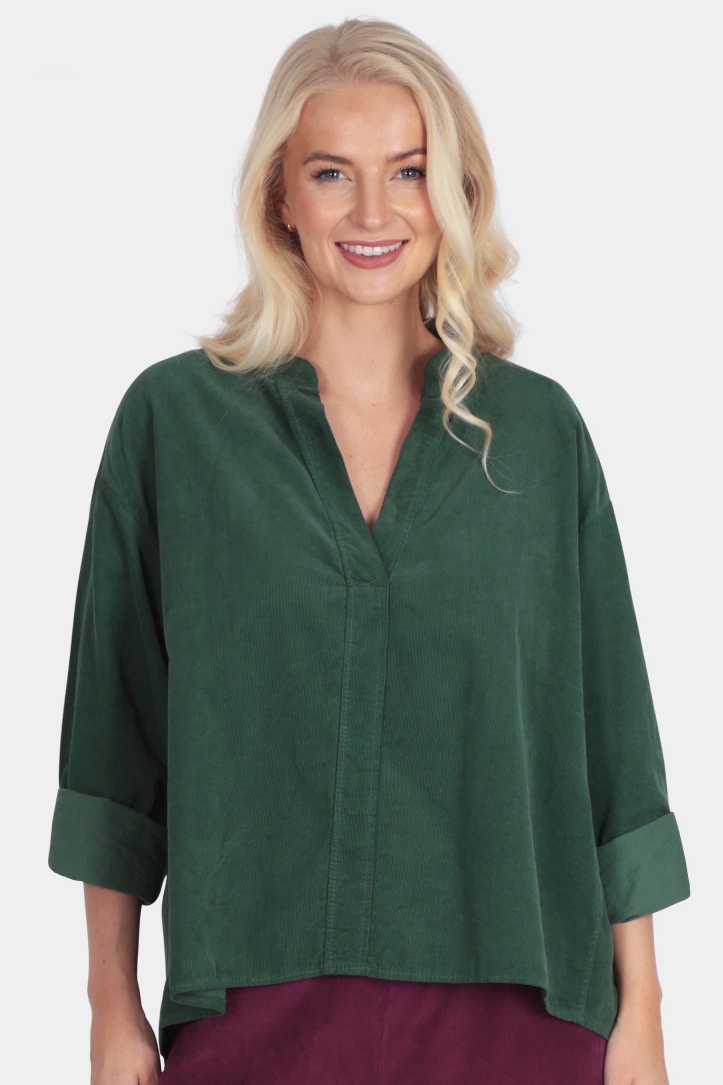 Woman wearing a green top and burgundy pants on a white background