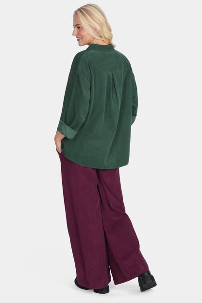 Woman wearing a green top and burgundy pants on a white background