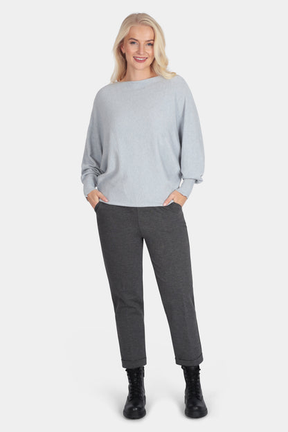 Woman wearing a light gray sweater and dark gray pants on a white background