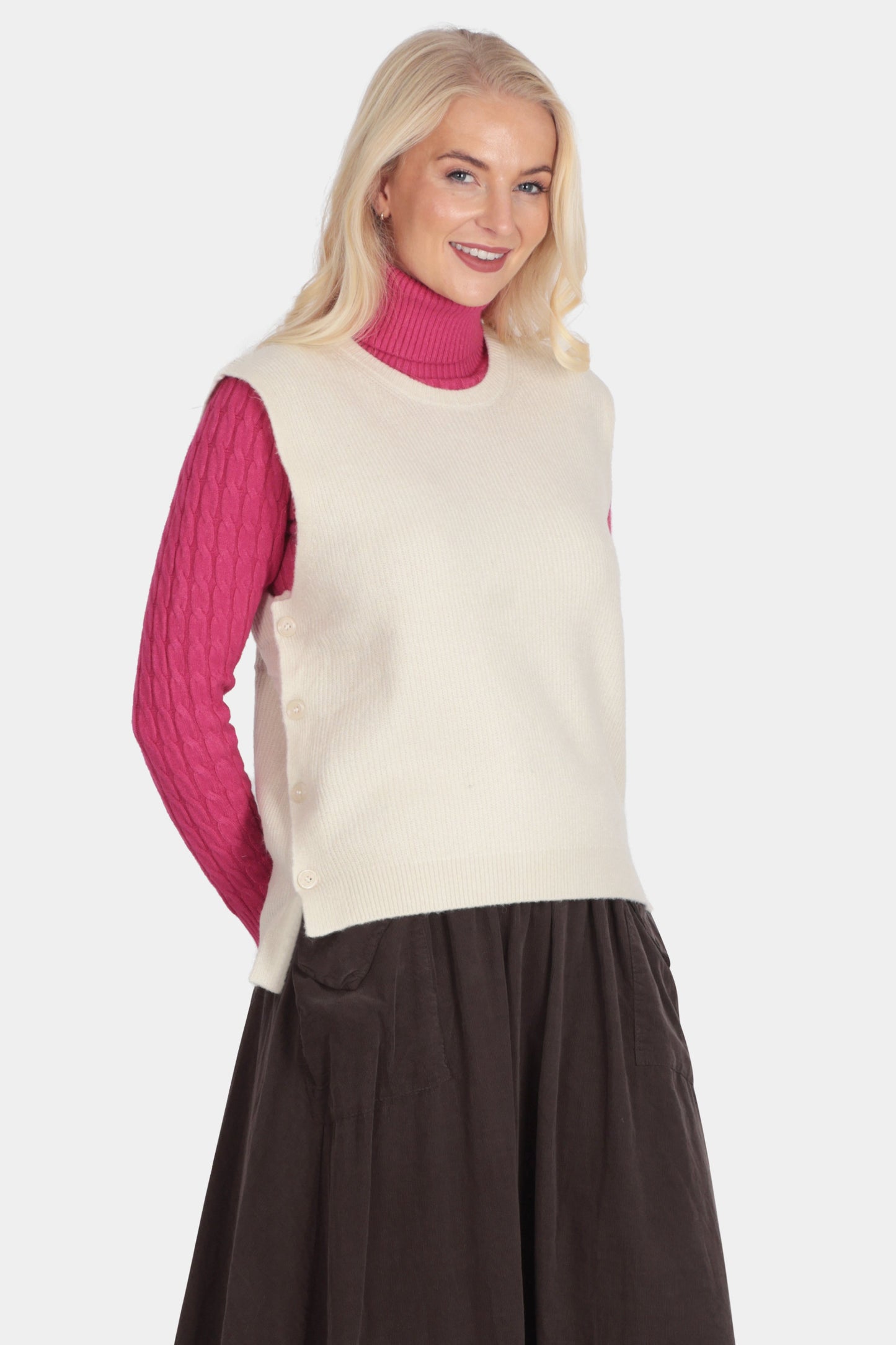 Woman wearing a cream vest over a pink sweater with a brown skirt on a white background