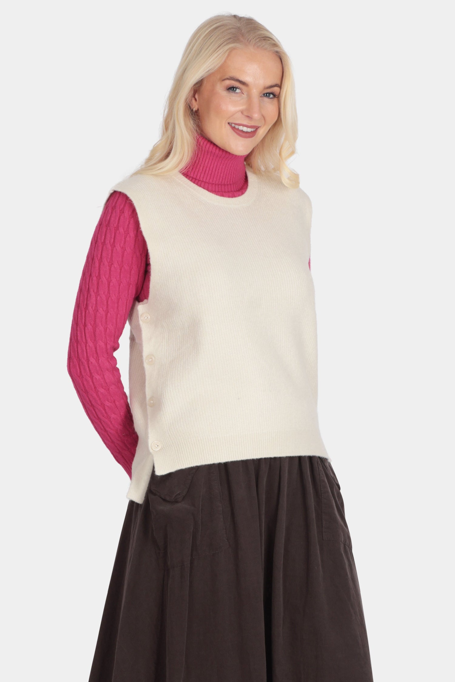 Woman wearing a cream vest over a pink sweater with a brown skirt on a white background