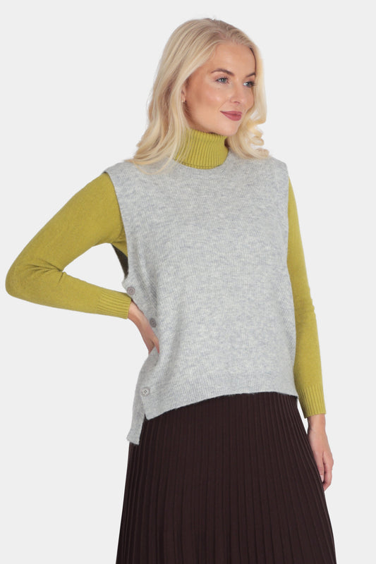 Woman wearing a green long-sleeve top, gray vest, and brown pleated skirt on a white background