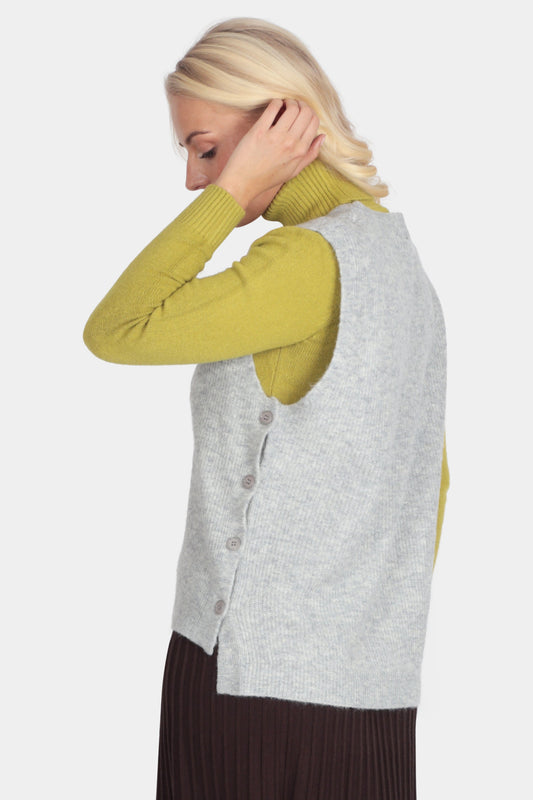 Woman wearing a gray vest over a green long-sleeve top and brown skirt on a white background