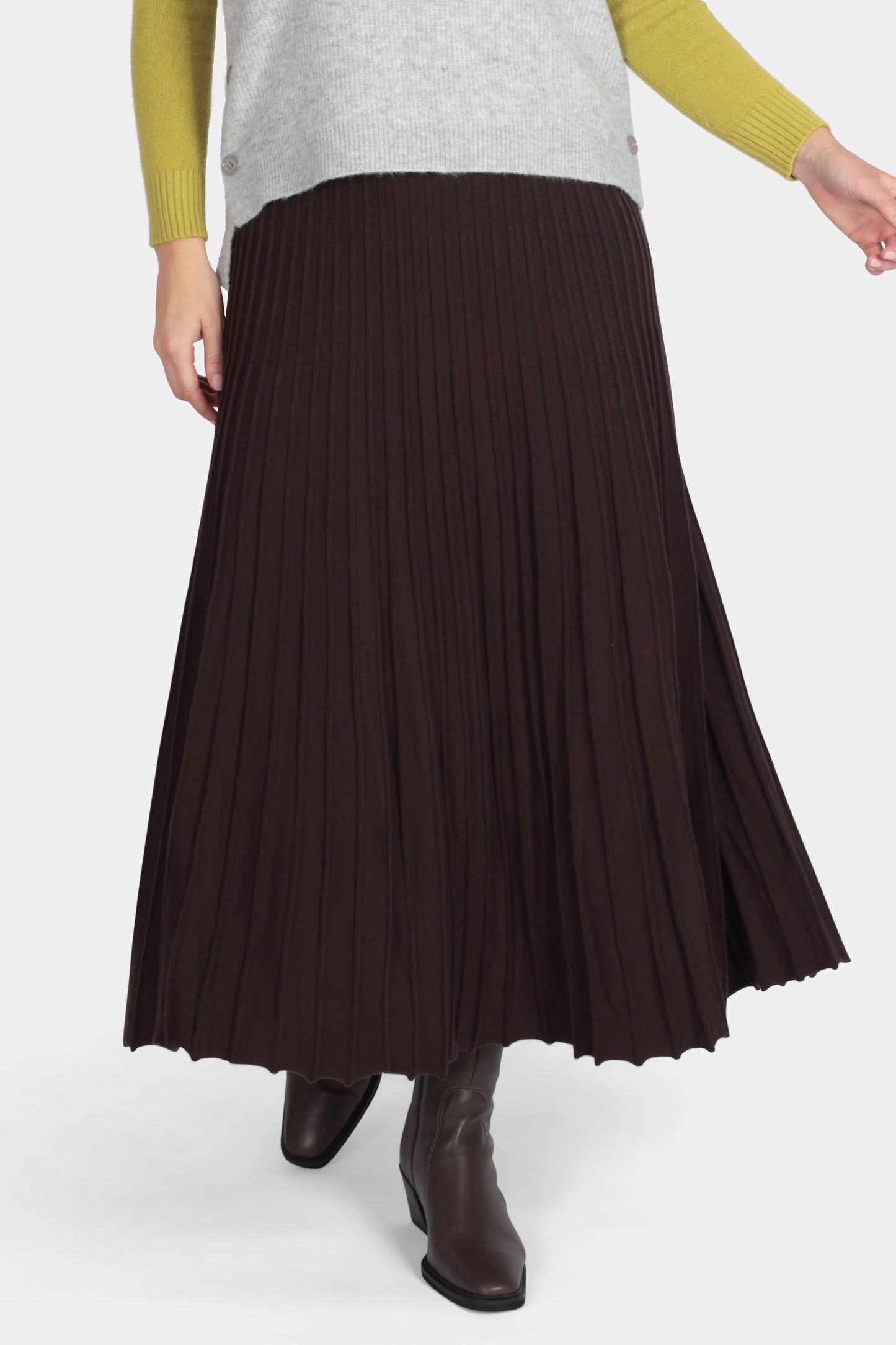 Woman wearing a sleeveless gray top, green long-sleeve shirt, and brown pleated skirt on a white background