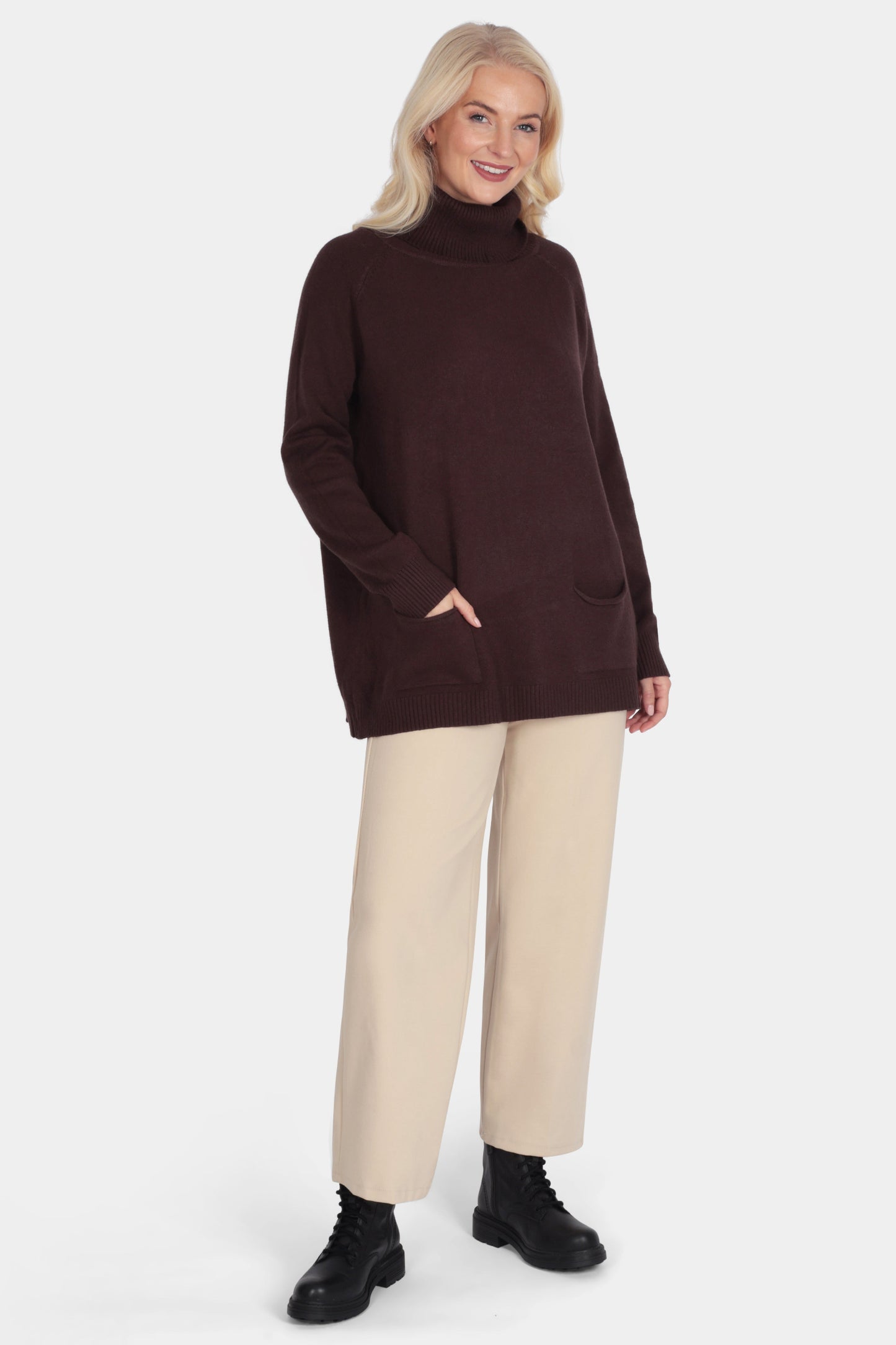 Woman wearing a brown turtleneck sweater and beige pants on a white background