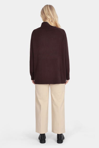 Person wearing a brown jacket and beige pants on a white background