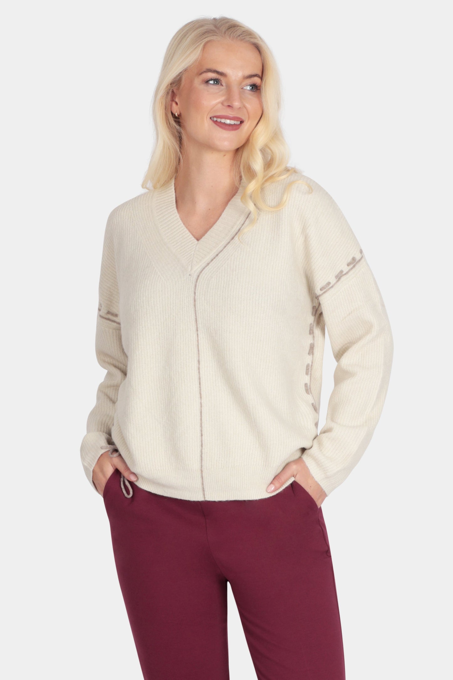 Woman wearing a cream sweater and burgundy pants on a white background