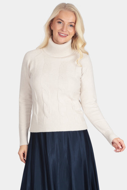 Woman wearing a cream turtleneck sweater and navy skirt on a white background