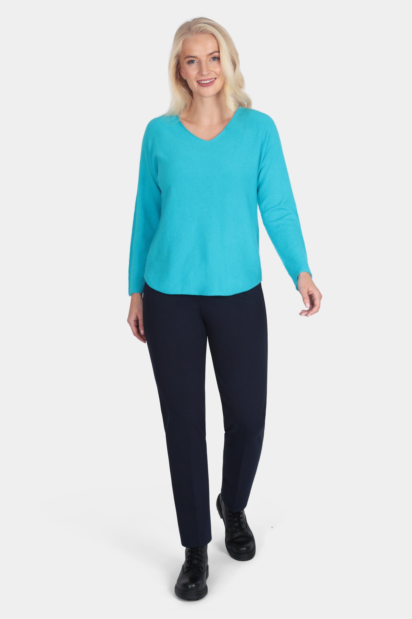 Woman wearing a turquoise long-sleeve top and black pants on a white background