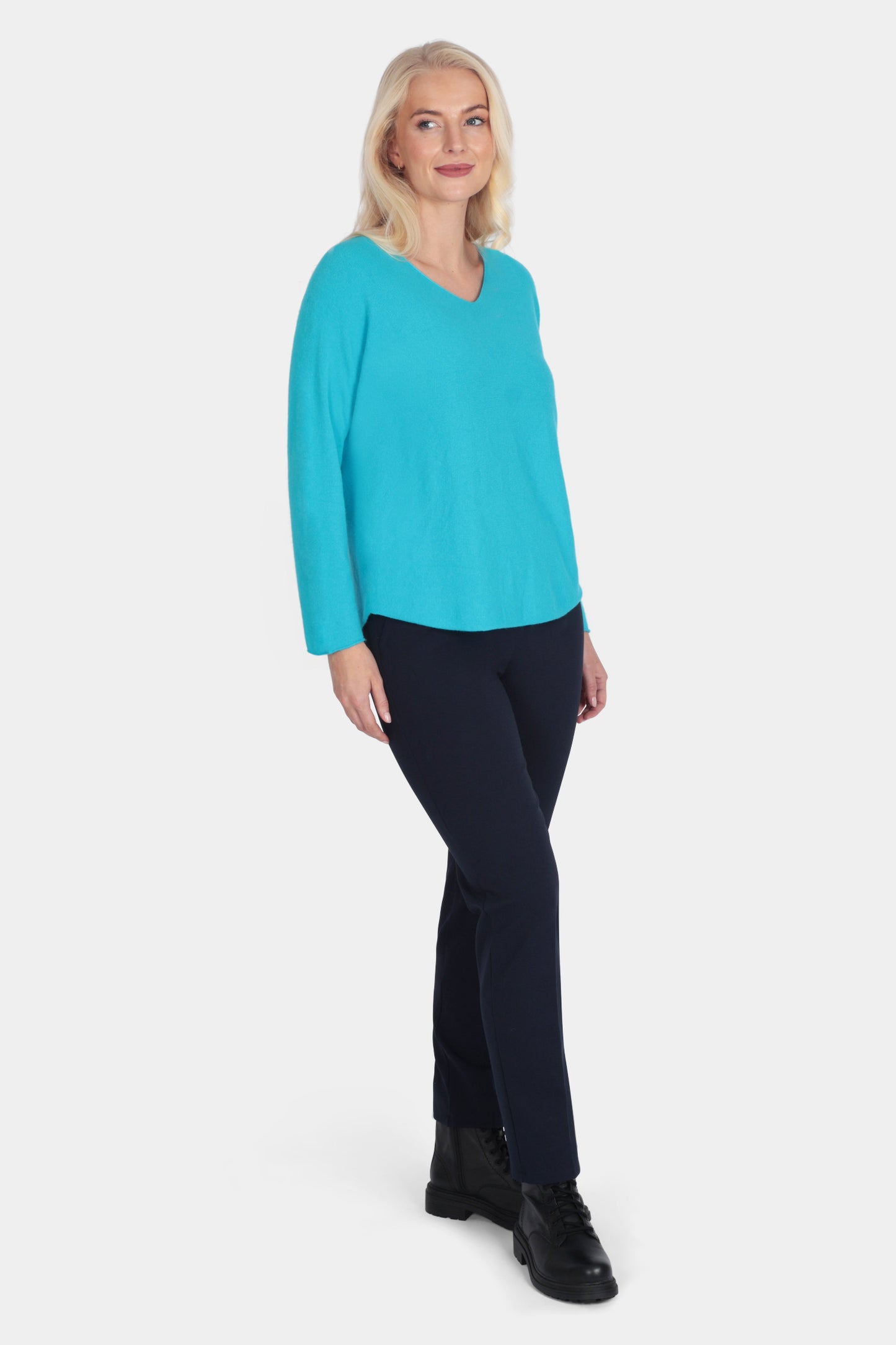 Woman wearing a turquoise sweater and black pants on a white background