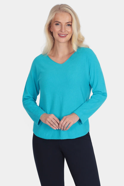 Woman wearing a turquoise sweater and black pants on a white background
