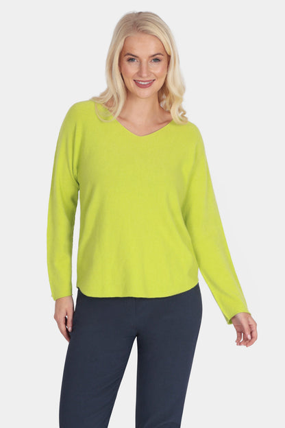 Woman wearing a bright green sweater and navy pants on a white background