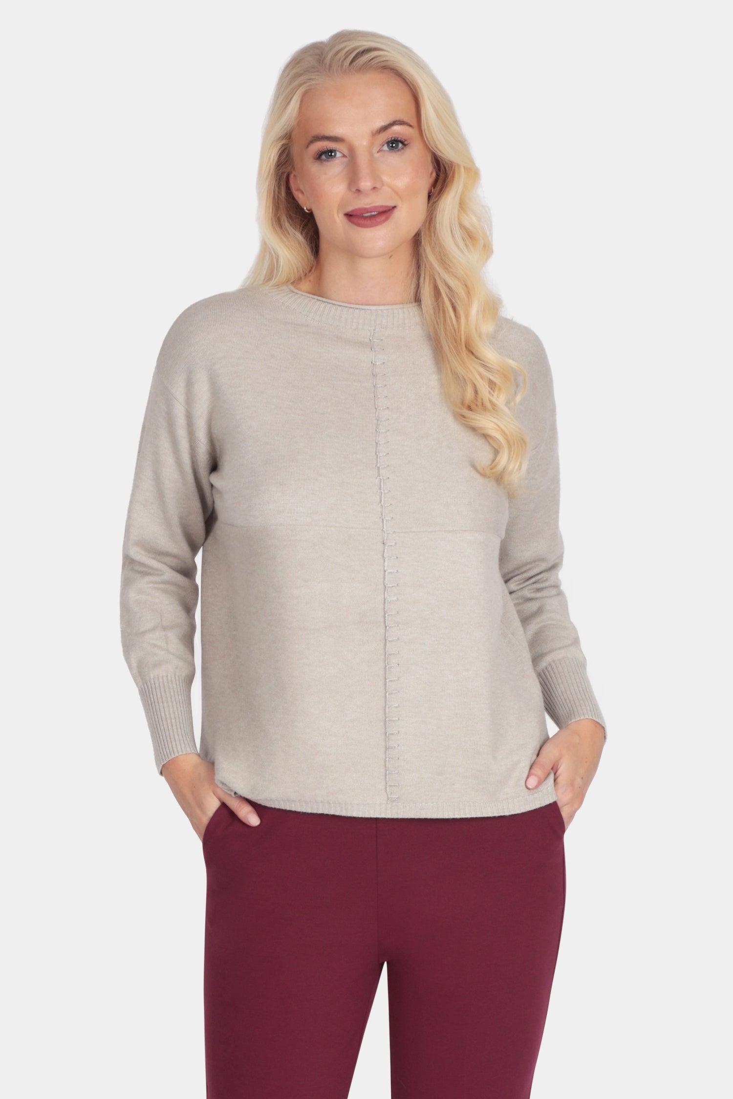 Woman wearing a beige sweater and burgundy pants on a white background