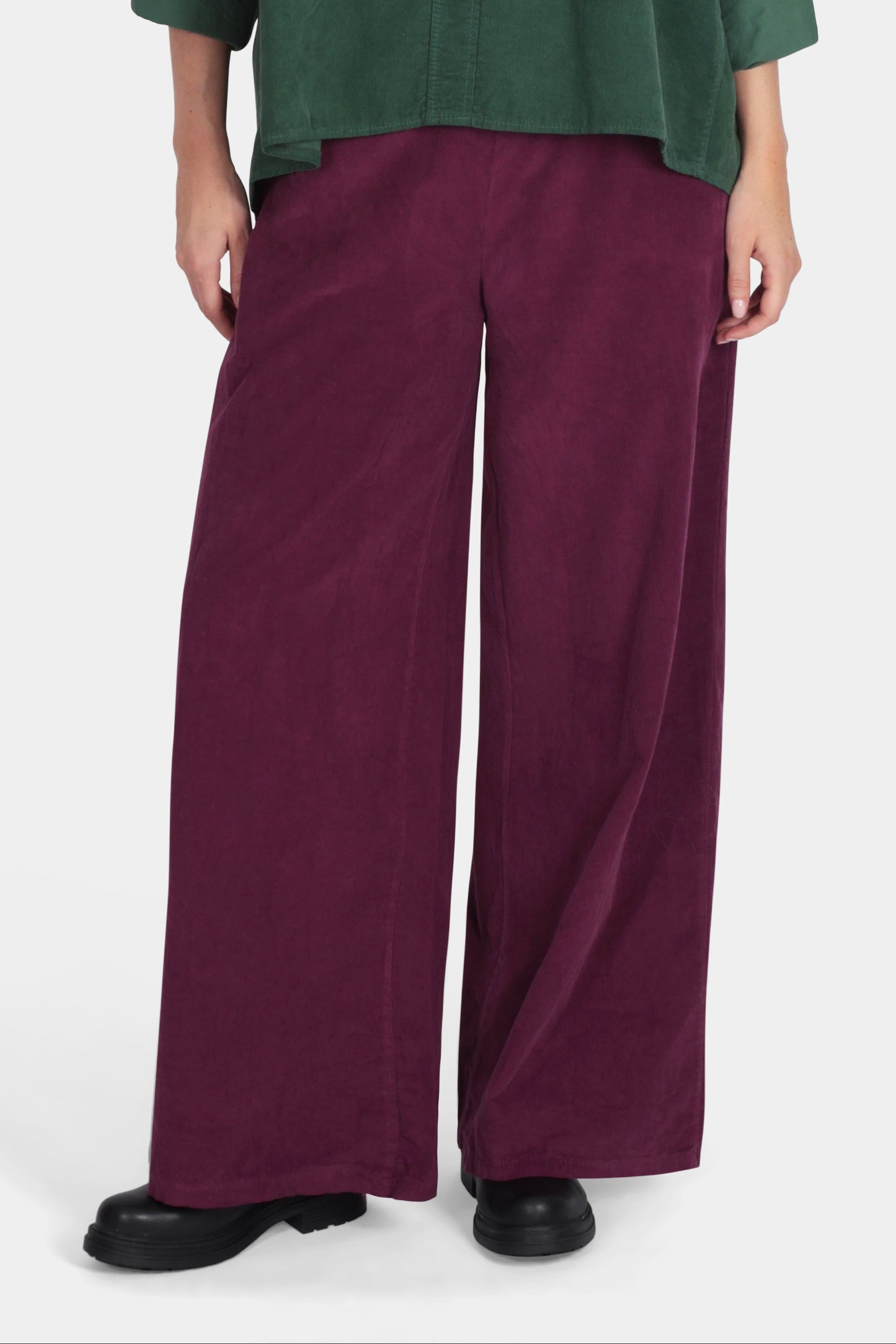 Woman wearing a green top and burgundy pants on a white background