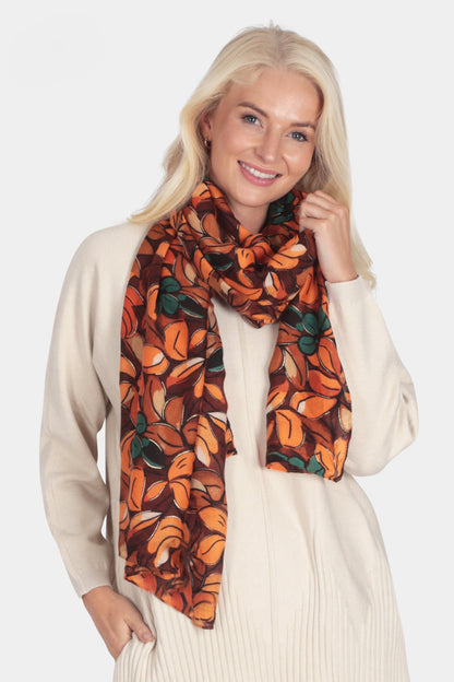 Woman wearing a beige sweater, brown pants, and an orange scarf with a pattern on a white background