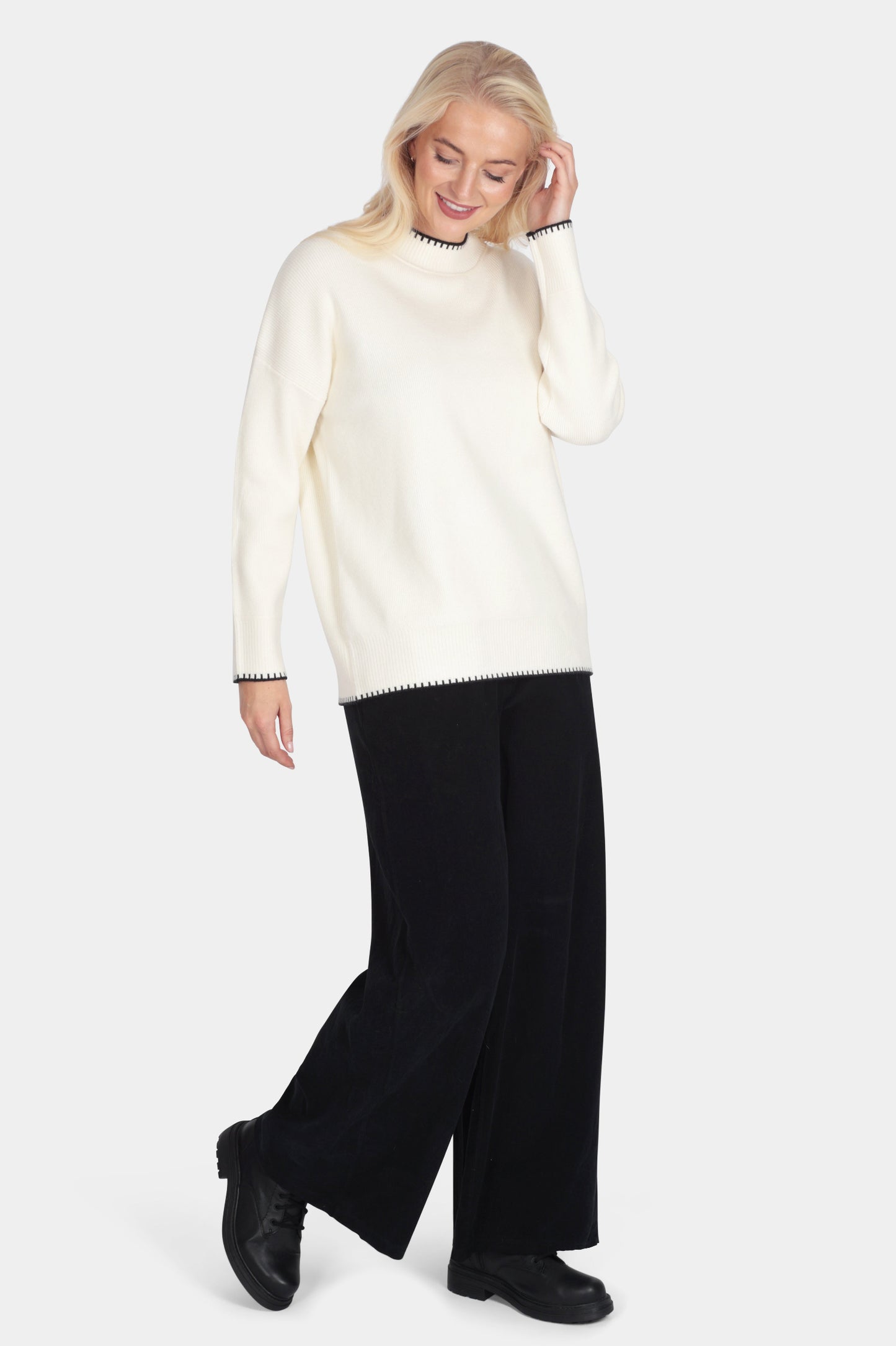 Woman wearing a cream sweater and black pants on a white background
