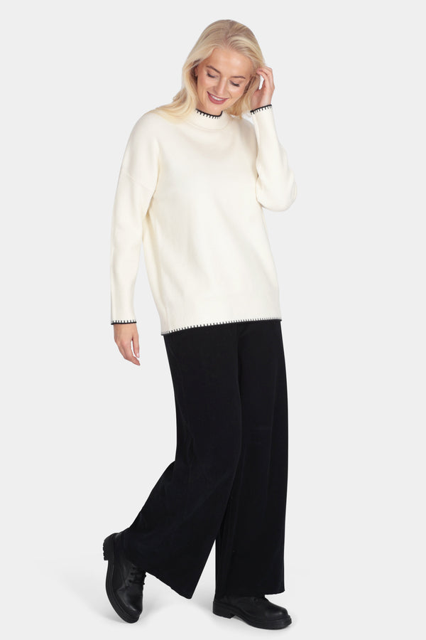Woman wearing a cream sweater and black pants on a white background