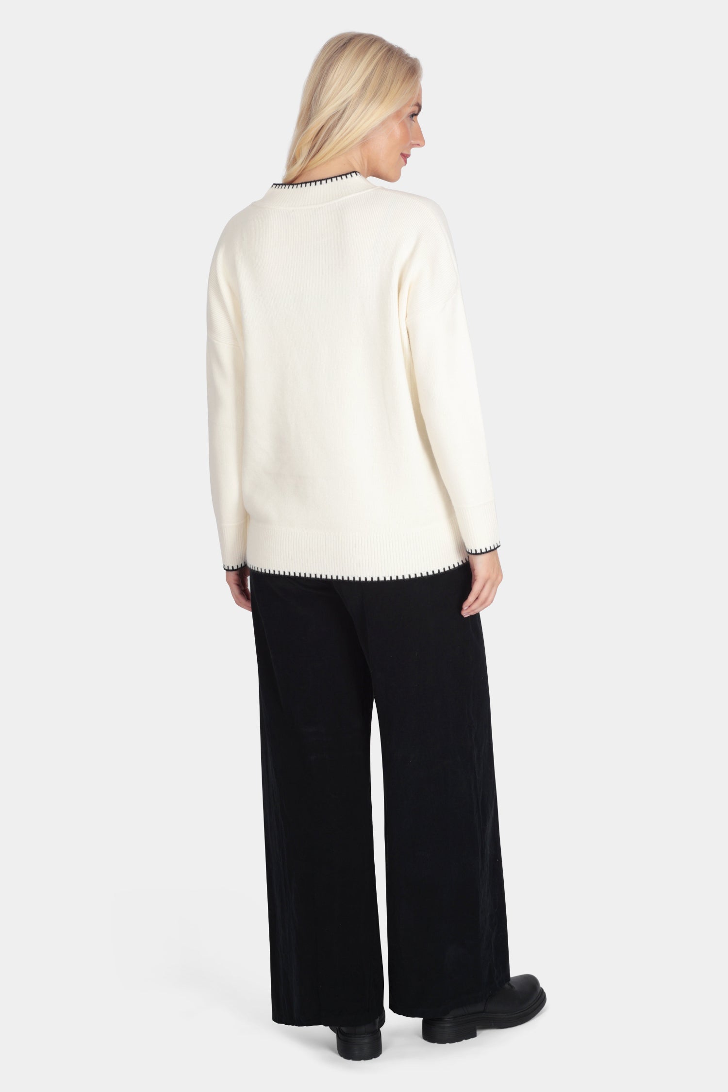 Woman wearing a cream sweater and black pants on a white background