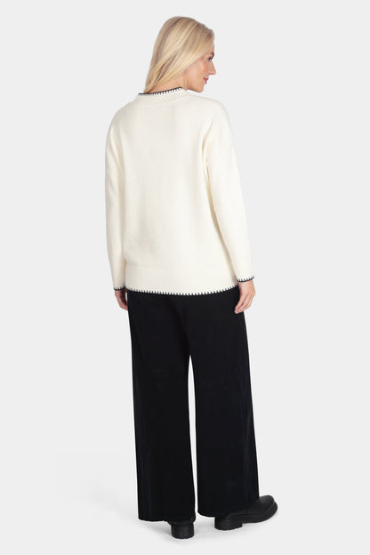 Woman wearing a cream sweater and black pants on a white background