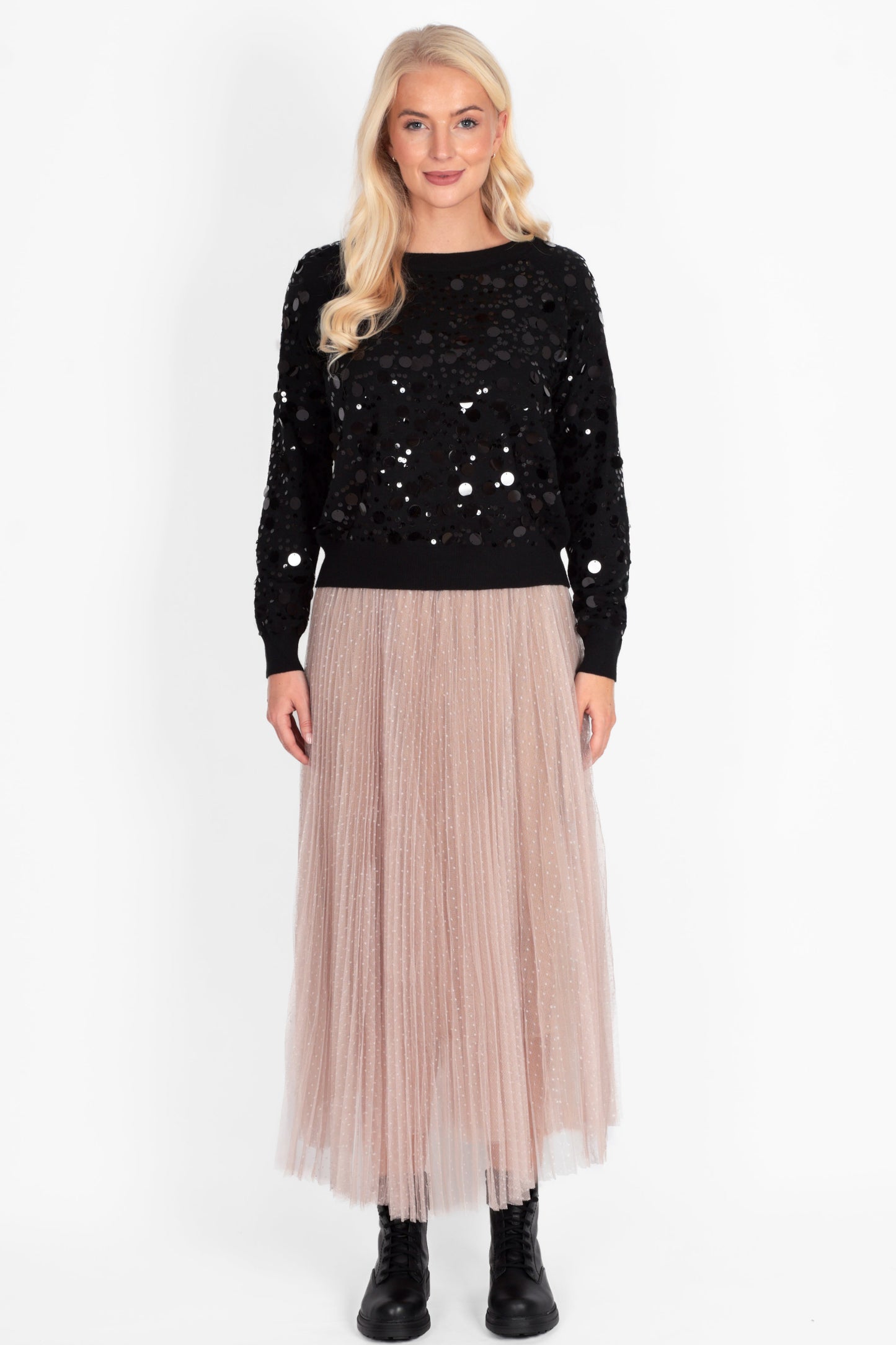 Woman wearing a black sequin top and beige pleated skirt on a white background