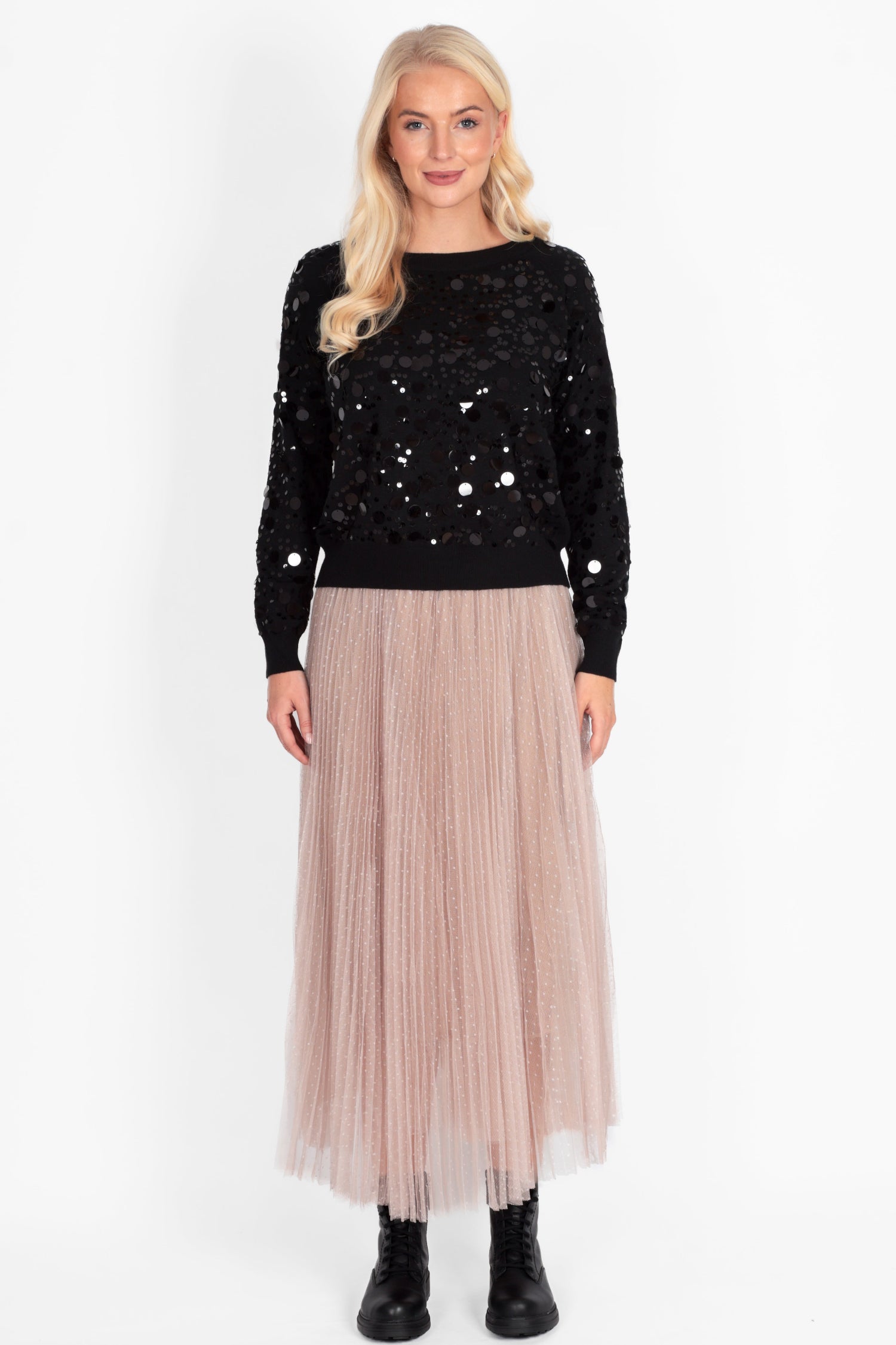 Woman wearing a black sequin top and beige pleated skirt on a white background