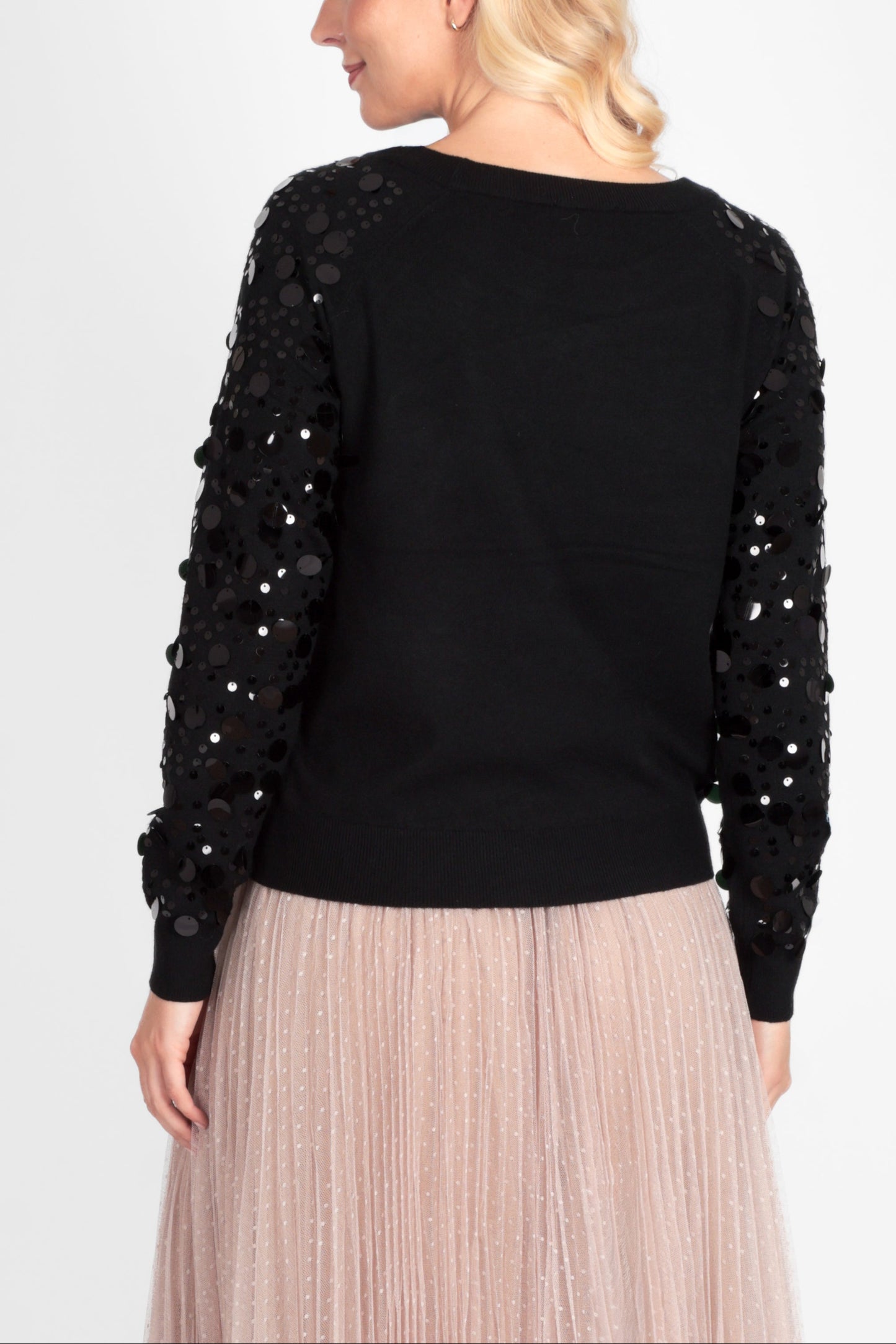 Woman wearing a black sweater with sequin details and a beige pleated skirt on a white background