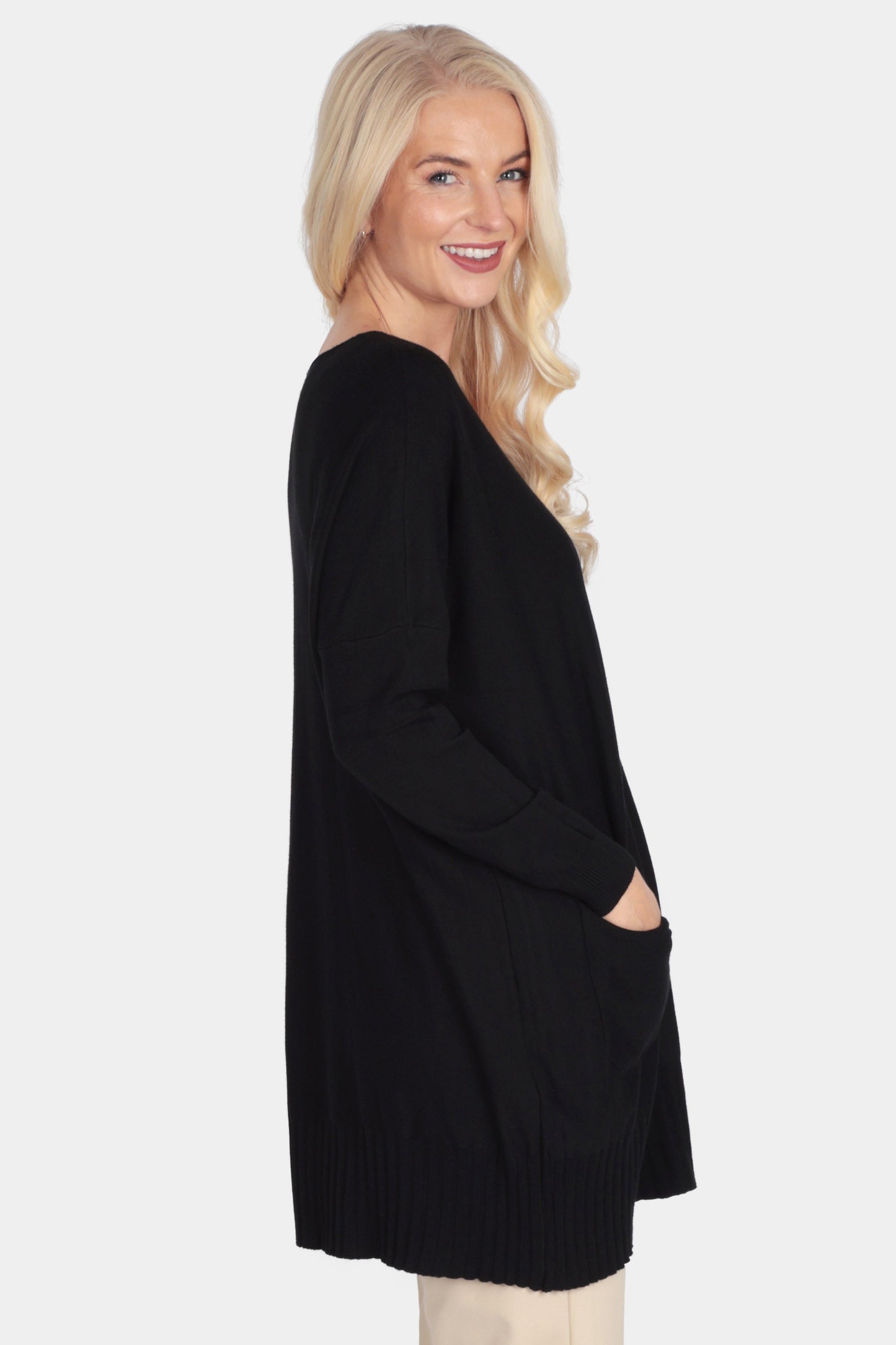 Woman wearing a black cardigan, beige pants, and black boots on a white background