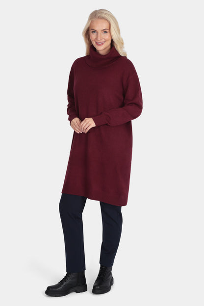 Woman wearing a burgundy tunic with black pants and shoes on a white background