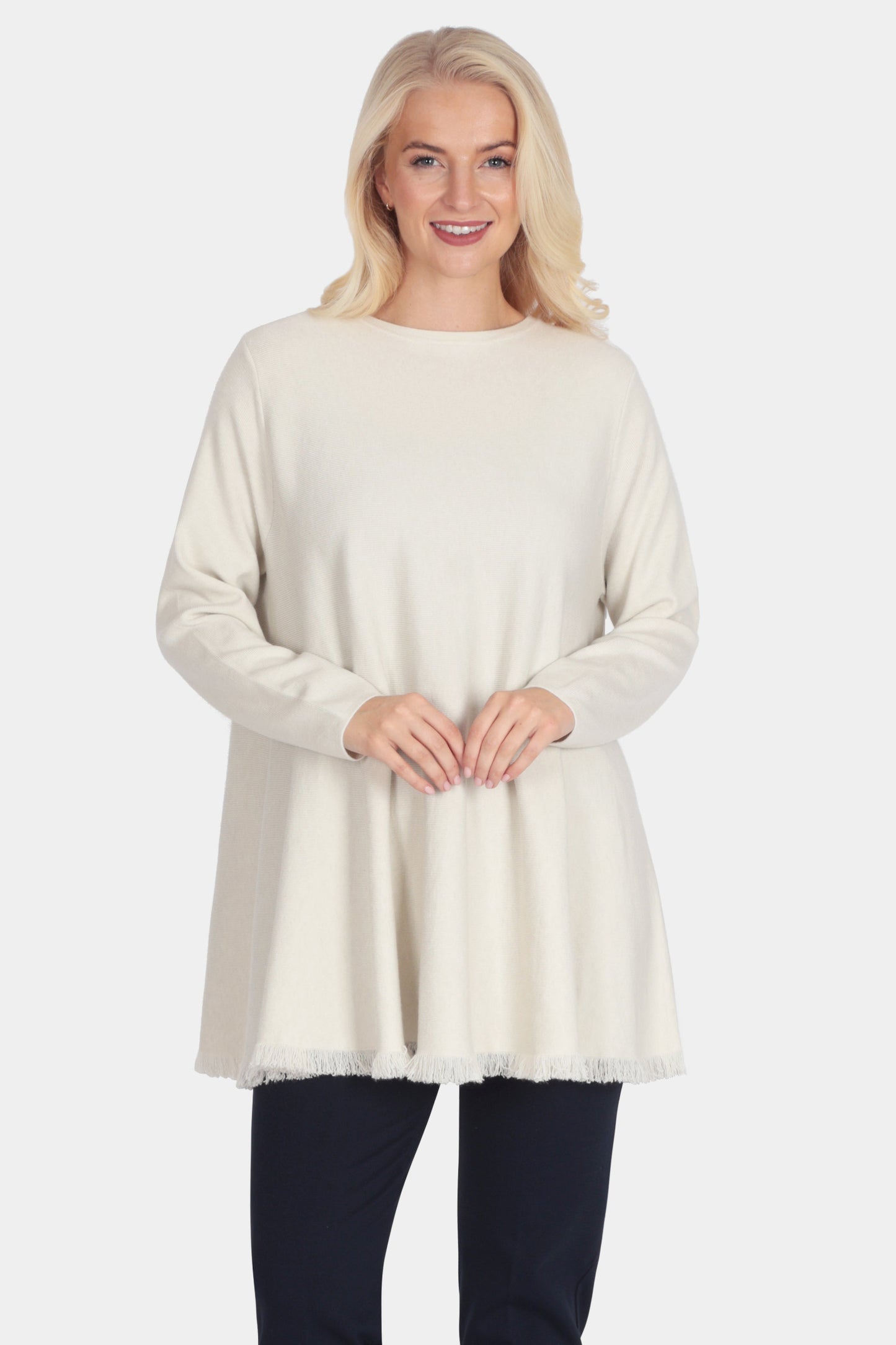 Woman wearing a cream sweater and black pants on a white background