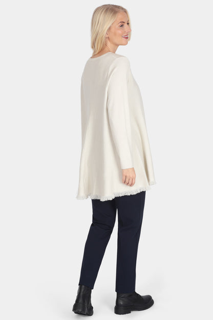 Woman wearing a white poncho over dark pants on a white background